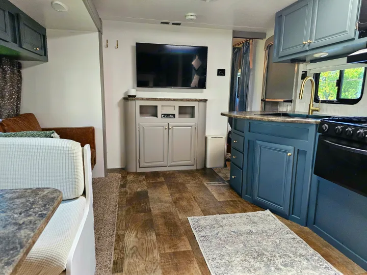 Modern RV rental interior: kitchen with blue cabinets, wood floor, living area with TV & dinette for your travels.. Crossroads RV Z-1 2017