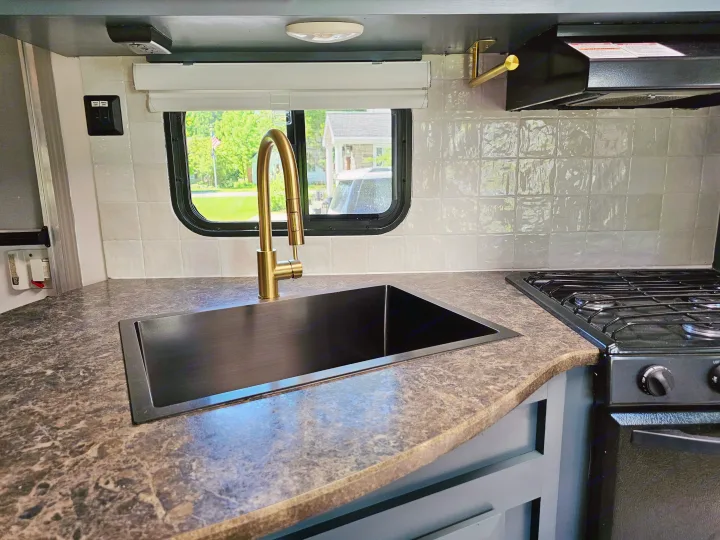 Clean RV rental kitchen with a black sink, brass faucet, tiled backsplash, and gas stove for cooking on the road.. Crossroads RV Z-1 2017
