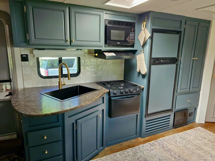Modernized RV kitchen interior features dark teal cabinets, gold hardware, tiled backsplash, and full appliances. Great for an rv rental.. Crossroads RV Z-1 2017
