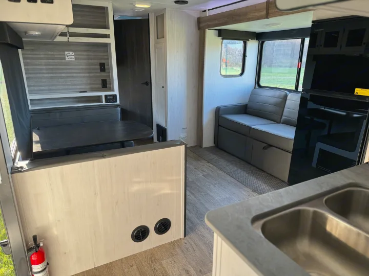 This RV rental interior features a dinette, sofa, and kitchen with a double sink, ready for travel adventures.. Heartland RVs Trail Runner 2023