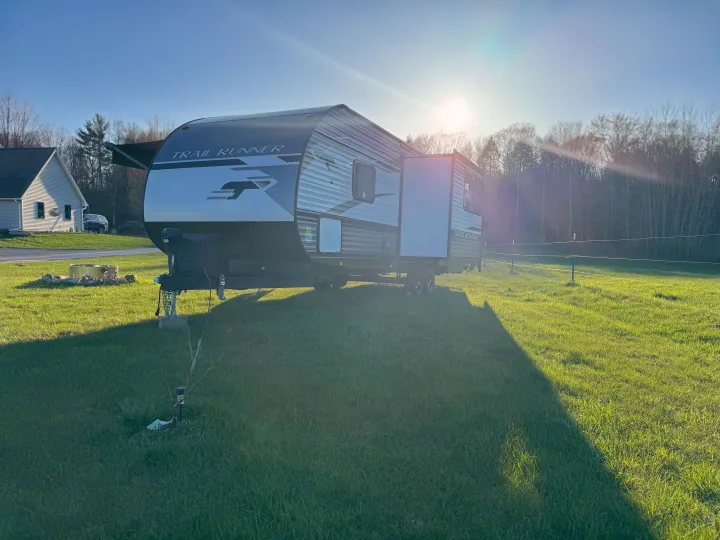 Travel trailer RV rental parked on a sunny green lawn with a fire pit. Perfect for camping!. Heartland RVs Trail Runner 2023