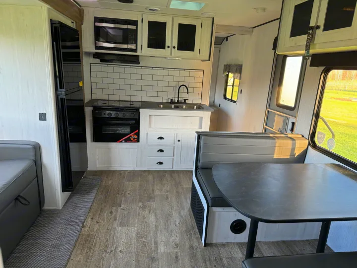 Clean RV rental interior: modern kitchen (microwave, fridge, subway tile), plus a comfy dinette with gray seating.. Heartland RVs Trail Runner 2023