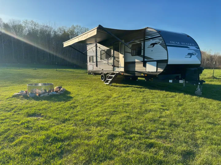 Spacious Trail Runner RV rental parked on a sunny green lawn with a fire pit, ready for a serene outdoor getaway.. Heartland RVs Trail Runner 2023
