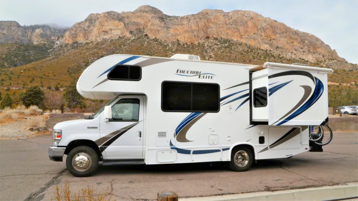 This white Freedom Elite rv rental is parked in nature with mountains in background. Slide-out extended, bikes ready.. Thor Motor Coach Freedom Elite 2018