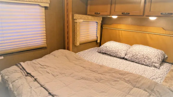 Step inside this cozy RV rental bedroom featuring a comfortable bed, overhead cabinets, and window blinds.. Thor Motor Coach Freedom Elite 2018