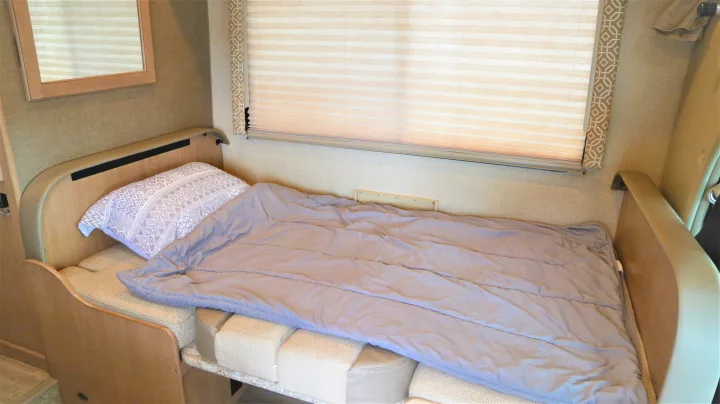 Cozy sleeping area in an rv rental, with a made-up bed, patterned pillow, and window blinds.. Thor Motor Coach Freedom Elite 2018
