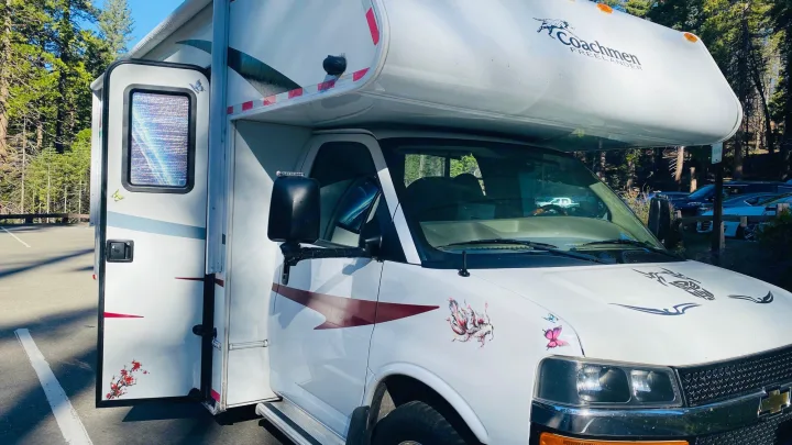 Explore nature with this white Coachmen Freelander RV rental. Parked among trees, it features custom decals and an open door.. Coachmam Freelander 21QB 2012