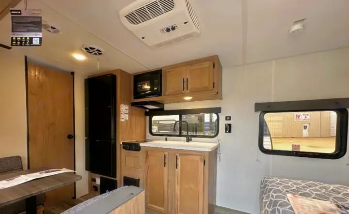 Inside this modern RV rental: a compact kitchen with a microwave, stove, sink, fridge, plus a dining area and sofa.. Forest River Cherokee Wolf Pup 2023
