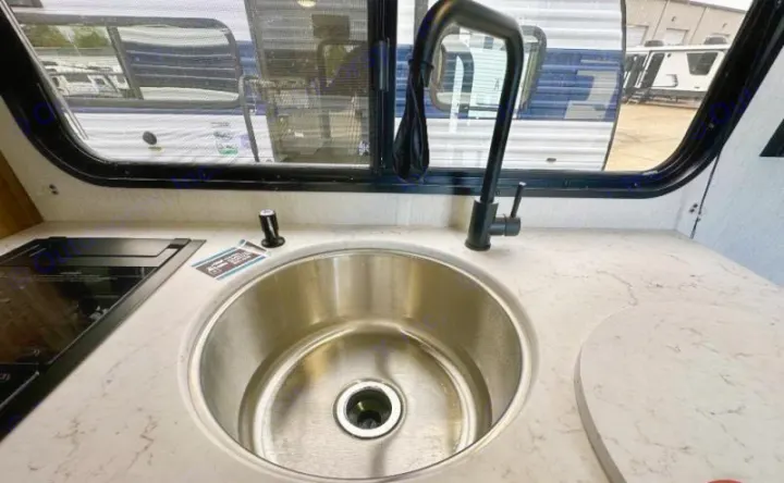 Inside an RV rental: a compact kitchen featuring a stainless steel sink, black faucet, and cooktop with a window view.. Forest River Cherokee Wolf Pup 2023