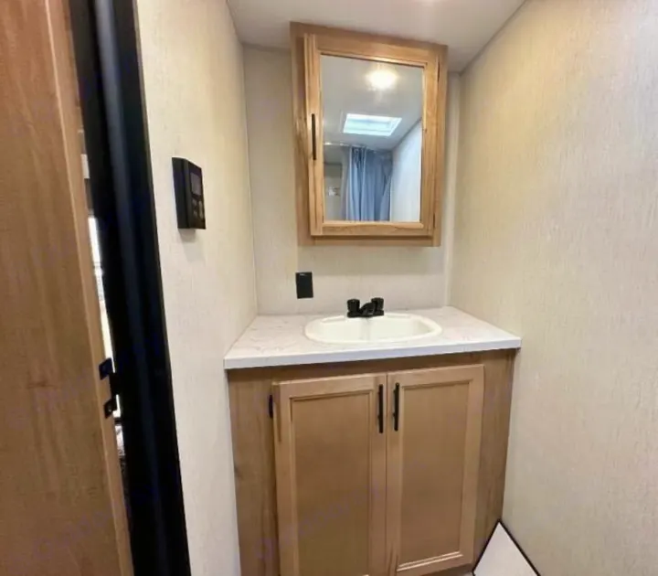 Functional RV rental bathroom with a compact light wood vanity, white sink, and mirrored medicine cabinet. Shower visible in reflection.. Forest River Cherokee Wolf Pup 2023