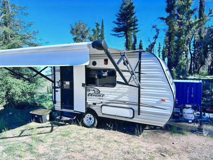 A white Jayco Flight travel trailer RV rental with an extended awning, parked in a sunny outdoor setting with trees.. Jayco Jay Flight SLX 2016