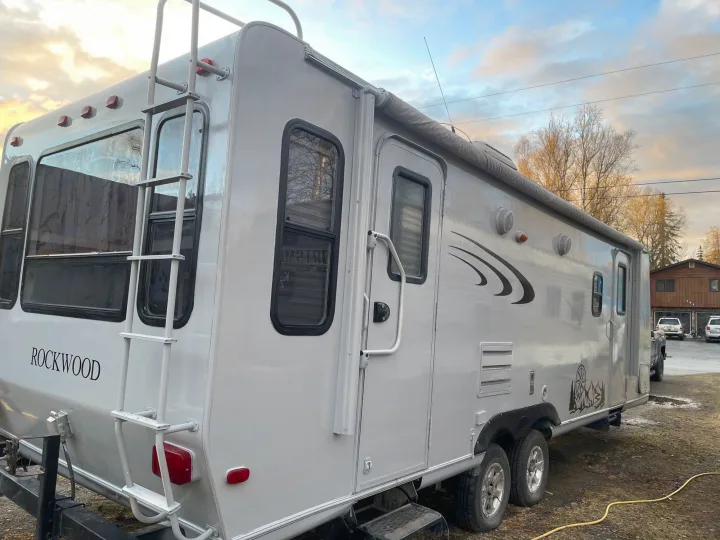 Grey Rockwood travel trailer, an ideal RV rental for outdoor adventures, parked outside with ladder & awning visible.. Forest River Rockwood Ultra Lite 2009