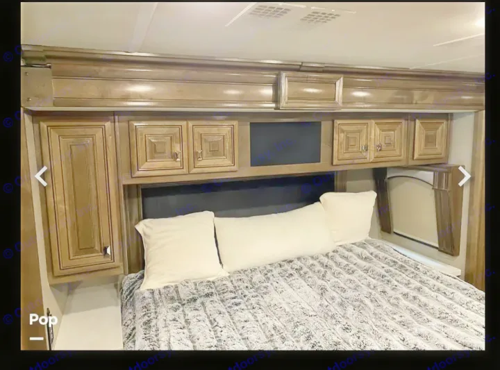 RV rental bedroom interior: cozy bed, overhead cabinets, and window. Ideal storage for travel.. Fleetwood Discovery LXE 2020