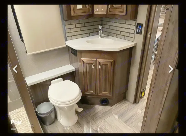 Modern RV rental restroom with corner sink vanity, toilet, and stylish gray tile backsplash.. Fleetwood Discovery LXE 2020