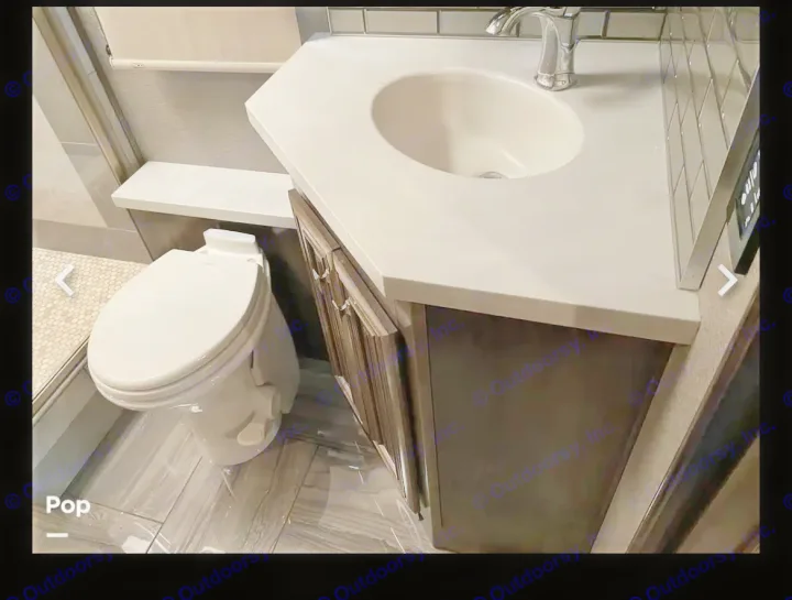 Modern RV rental bathroom with white toilet, dark vanity, sink, chrome faucet, and tiled shower area. Clean and functional design.. Fleetwood Discovery LXE 2020
