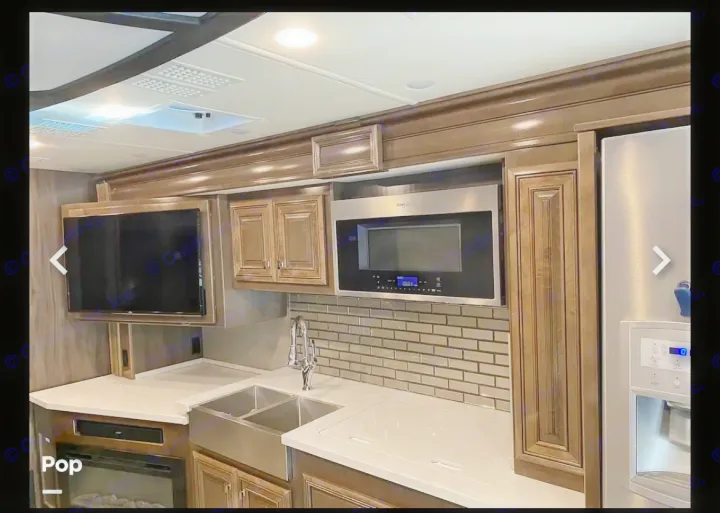Luxurious RV rental kitchen featuring a microwave, farmhouse sink, refrigerator, TV, and fireplace.. Fleetwood Discovery LXE 2020