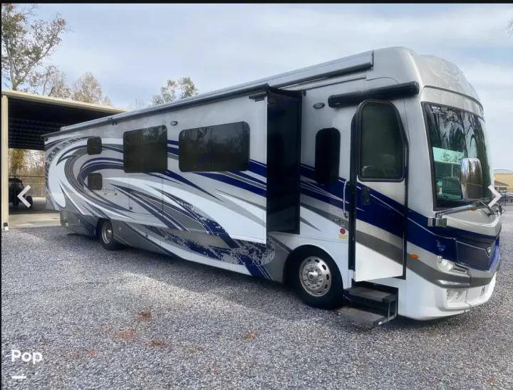 Spacious silver, blue, & white RV motorhome with open door & steps, parked on gravel. Perfect for an RV rental adventure.. Fleetwood Discovery LXE 2020