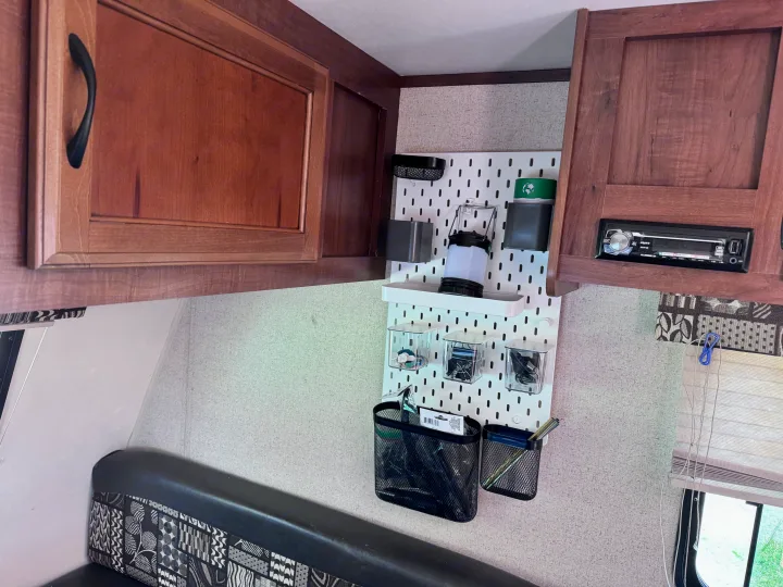 Inside an RV rental: view of organized storage with a white pegboard, wooden cabinets, and a patterned bench seating area.. Jayco Jay Flight SLX 2016
