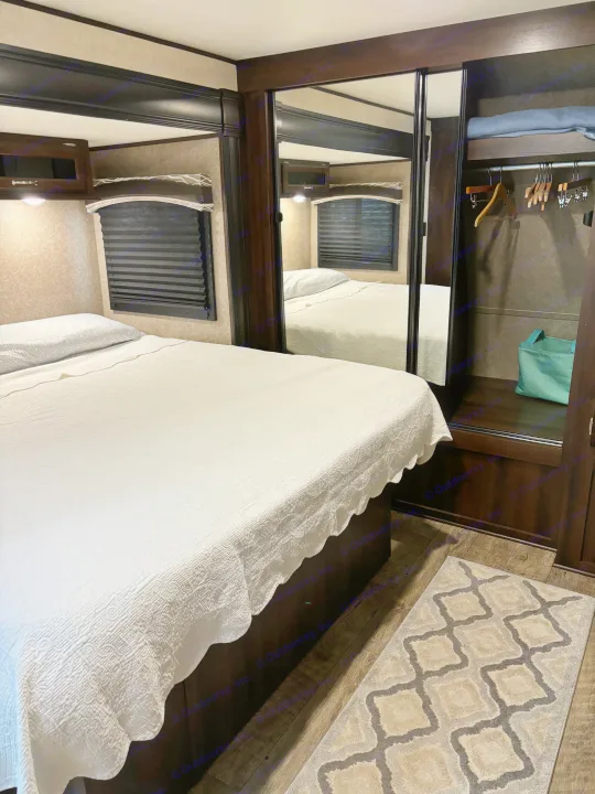 Cozy RV rental bedroom with white bedding, dark wood accents, a mirrored closet, and patterned rug. Perfect for travel.. Jayco Jay Flight 2018