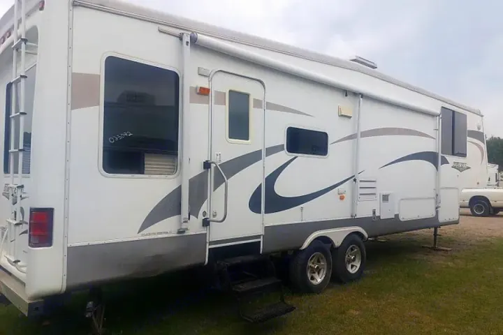 White camper RV rental, with an entry door, multiple windows, and a rear ladder, parked outdoors.. Crossroads Silverado 2005