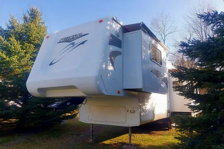A large white fifth-wheel RV, with "Silverado" branding, parked among evergreen trees.. Crossroads Silverado 2005