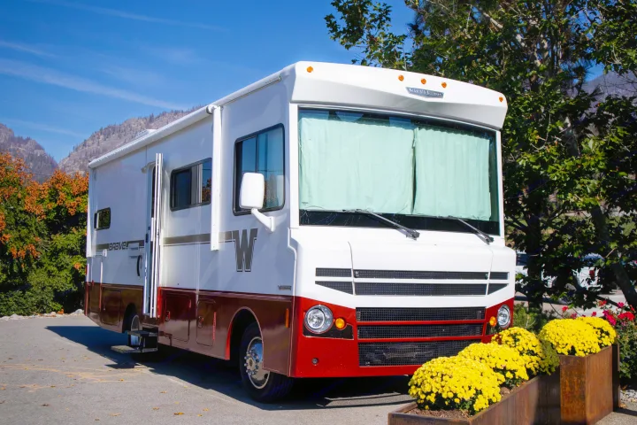 White and red Winnebago RV rental parked outdoors. Features yellow flowers in planters, mountains, and blue sky.. Winnebago Brave 2015