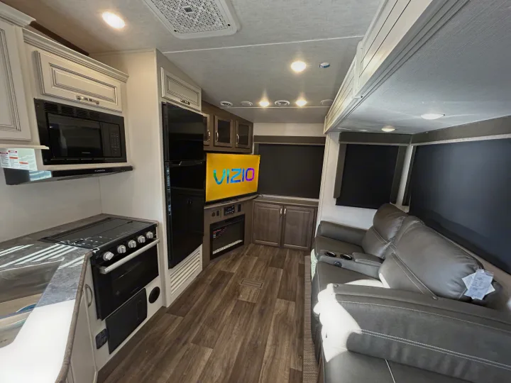 Inside a spacious RV rental: kitchen with microwave/stovetop, lounge area featuring a Vizio TV, fireplace, and recliners.. Keystone RV Cougar 2023