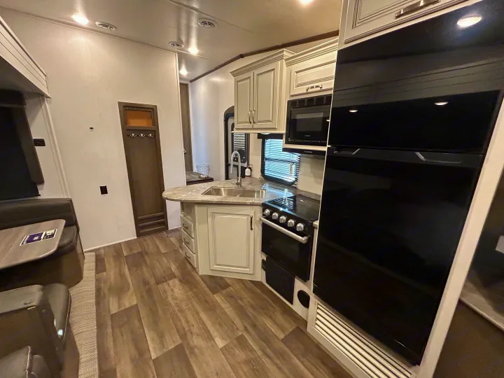 RV rental interior: A modern kitchen with light cabinets, appliances, and sink, next to a dining area with wood flooring.. Keystone RV Cougar 2023