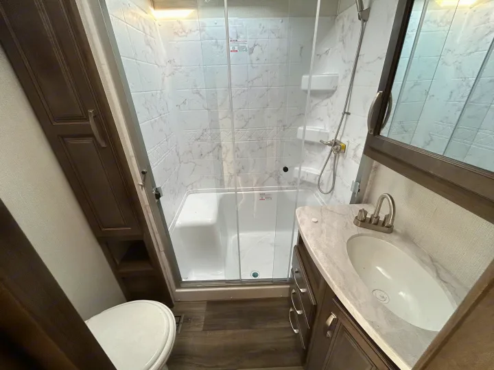 Modern RV rental bathroom: walk-in shower with bench, toilet, and vanity with sink. Compact and functional design.. Keystone RV Cougar 2023