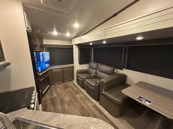 Cozy RV rental interior: living space with recliners, TV, fireplace, and dining booth. Modern design.. Keystone RV Cougar 2023