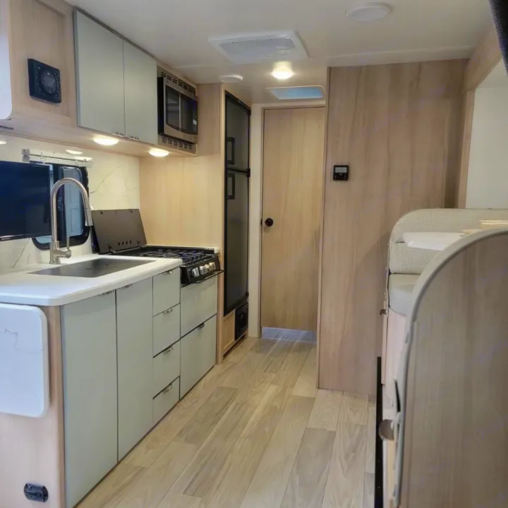 This RV rental's modern interior features a light gray kitchen with a sink, stove, and microwave, plus light wood flooring.. Minnie Micro Minnie 2023