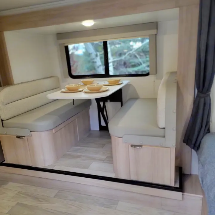 Bright RV rental dinette featuring light wood, grey cushions, a white table with bowls, and a window view.. Minnie Micro Minnie 2023