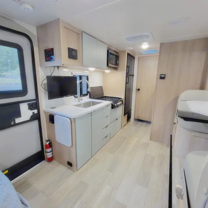 Modern RV rental kitchen area: light cabinetry, sink, stove, microwave, and fridge.. Minnie Micro Minnie 2023