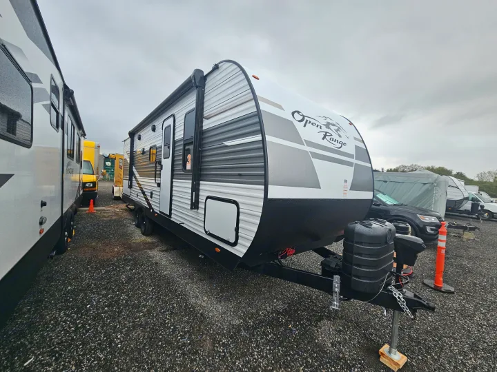 An Open Range travel trailer, ideal for RV rental, shown parked on a gravel lot under an overcast sky.. Highland Ridge RV Open Range 2024