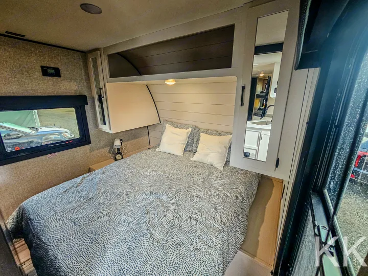 Cozy RV rental bedroom with patterned bedding, bedside lamp, and mirrored storage, offering comfort on the road.. Highland Ridge RV Open Range 2024