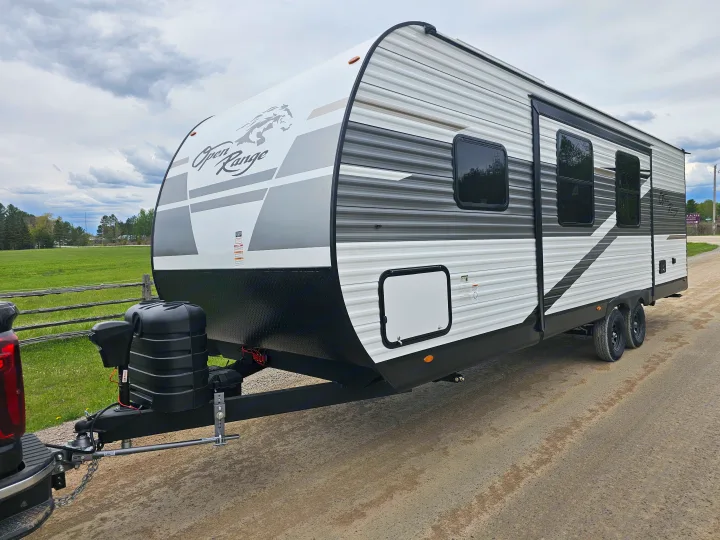 White & gray Open Range travel trailer (RV) on a dirt road, ready for rental trips.. Highland Ridge RV Open Range 2024