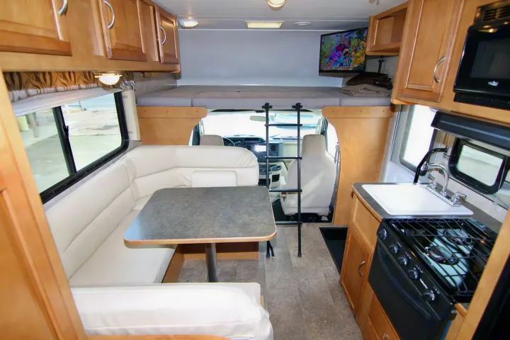 View inside an RV rental showing a comfy dinette, full kitchen, and front bunk bed with TV.. Winnebago Minnie Winnie 2016