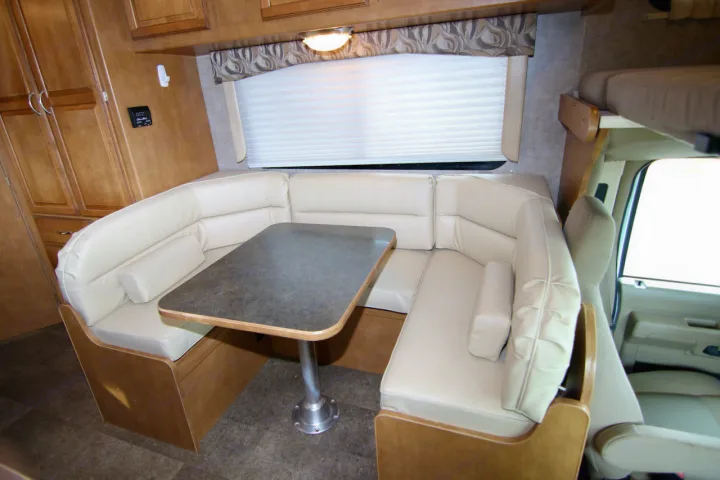 This RV rental interior features a cream U-shaped dinette, a sturdy table, wood cabinetry, and a window for comfort.. Winnebago Minnie Winnie 2016