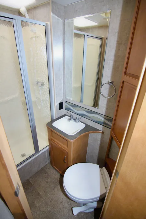 Compact RV rental bathroom: shower with glass doors, sink, toilet, mirror & storage. All essentials in one space.. Winnebago Minnie Winnie 2016