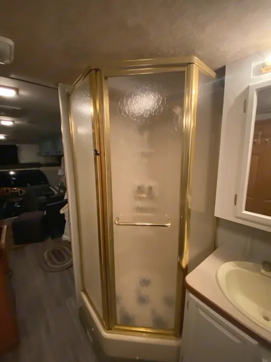 Functional RV rental bathroom featuring a corner shower with frosted glass & gold trim, plus a vanity & sink.. Coachmen Santara 2002