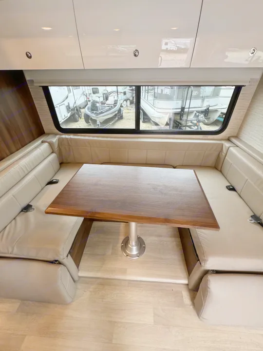 Spacious RV rental dinette featuring light-toned seating, a wooden table, and large windows revealing outdoor vehicles.. Winnebago View 2022