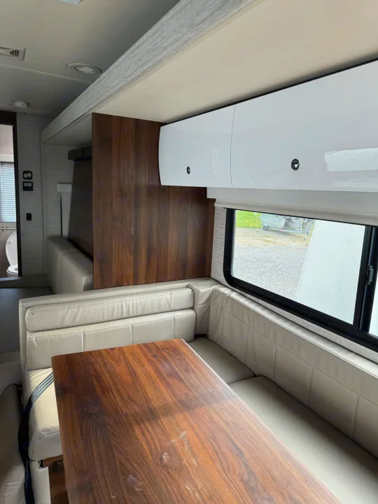 Step inside this RV rental's cozy dinette: a warm wood table, light-toned cushioned seating, and white overhead cabinets. Bathroom visible.. Winnebago View 2022