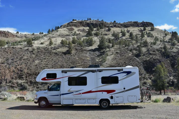 A white **rv rental** is parked in a scenic, arid landscape with hills and sparse trees. Bicycles are mounted on the rear rack, ready for adventure.. Forester Forester Motorhome 2019