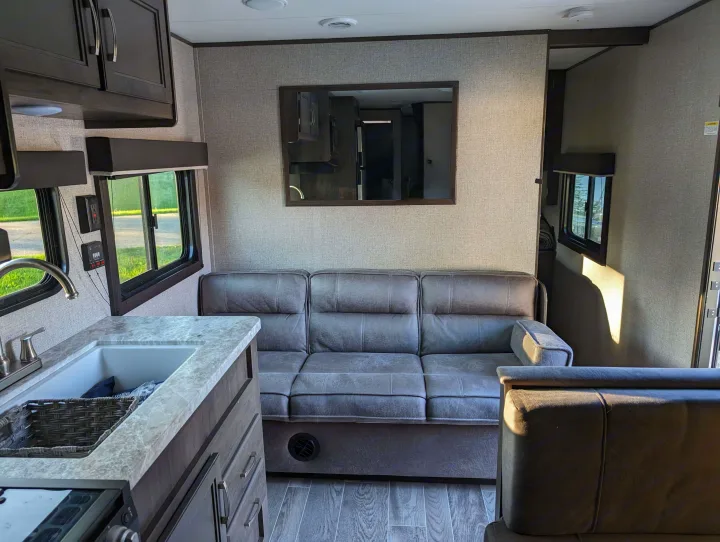 Spacious RV rental interior featuring a modern kitchen with sink, comfy gray sofa, and large windows with outdoor views.. Jayco Jay Flight SLX 2021