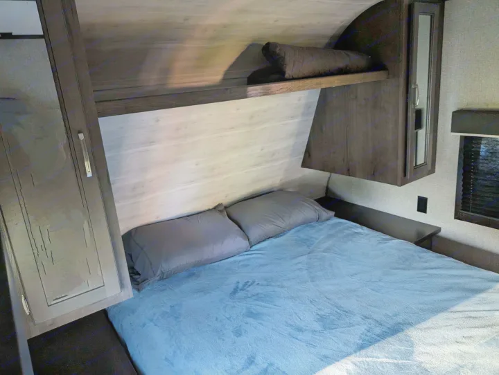Inside a comfy RV rental bedroom, featuring a light blue bed, grey pillows, and dark wood storage.. Jayco Jay Flight SLX 2021