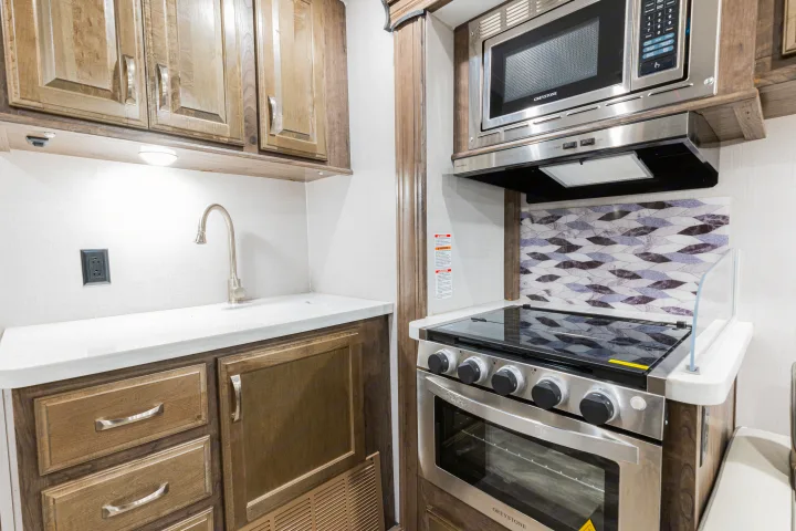 Modern RV rental kitchen featuring light wood cabinets, white counters, stainless steel microwave, and oven.. Gulf Stream Yellowstone 2023