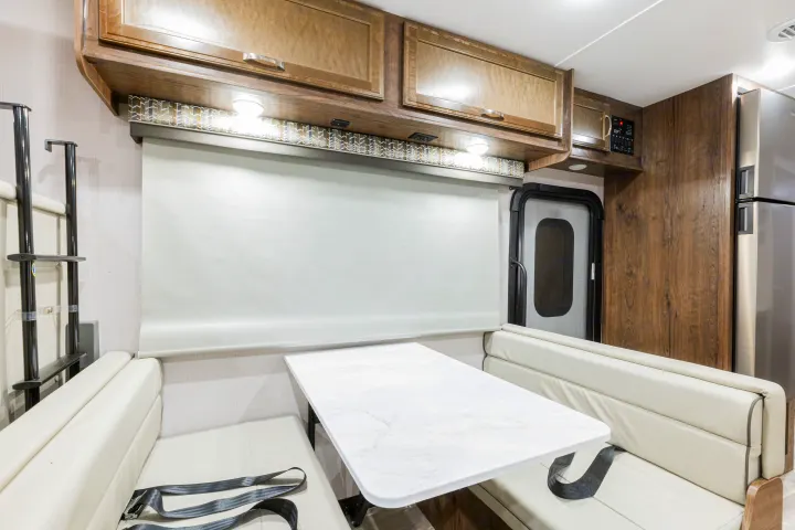 Modern rv rental interior: bright dinette with a marble table, cream benches, overhead storage, and window blind.. Gulf Stream Yellowstone 2023