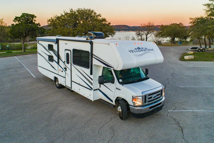 White Yellowstone RV rental in a parking lot, with a scenic lake, trees, and sky at dusk in the background.. Gulf Stream Yellowstone 2023