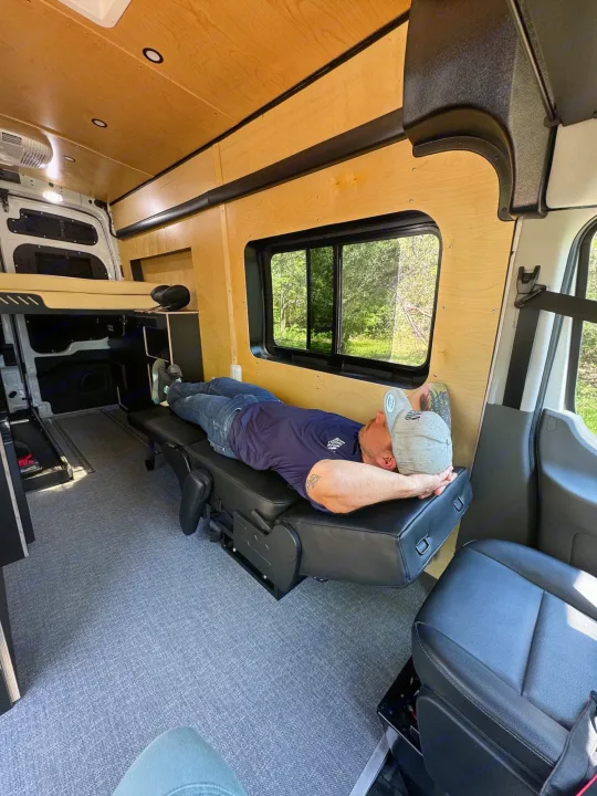 Inside an RV rental: Man relaxes on a modular seat in this custom camper van conversion.. Ford Transit 2023
