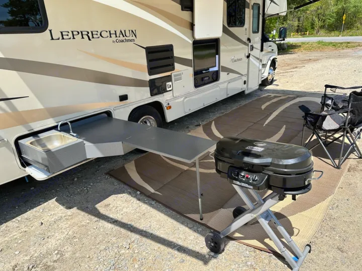 RV rental with a convenient pull-out outdoor kitchen, sink, and grill setup at a sunny campsite for an enjoyable trip.. Coachmen Leprechaun 2019